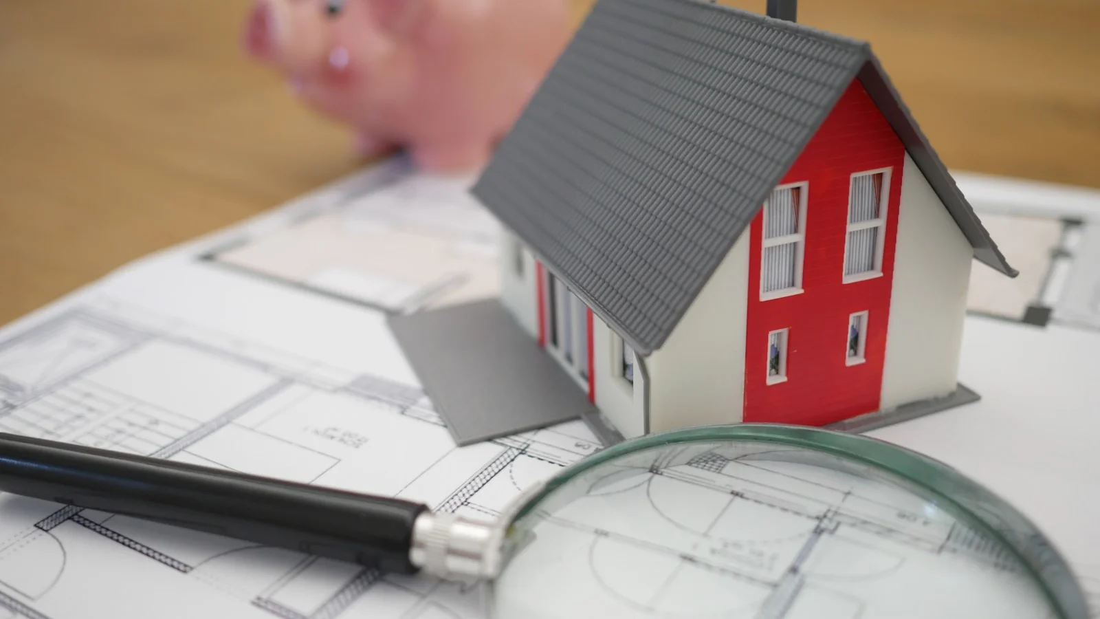 Maison miniature rouge et blanche posée à côté d'une loupe sur une surface claire